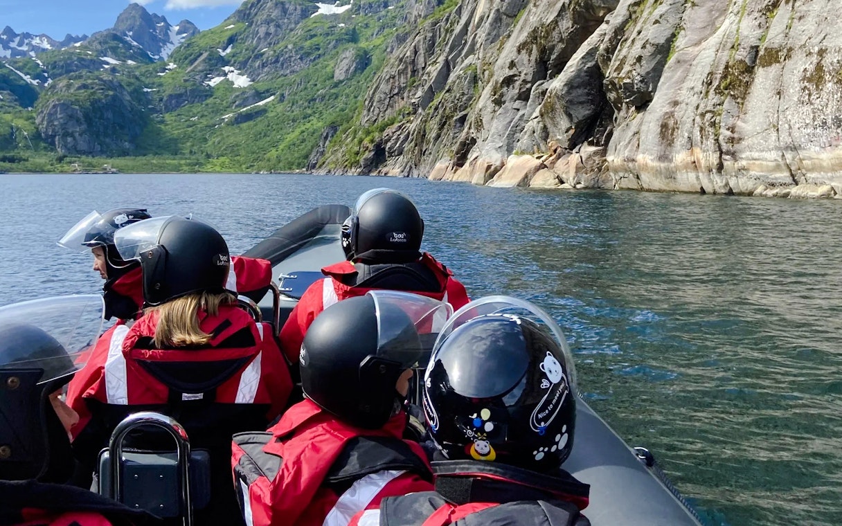 RIB boat tour in Lofoten with passengers in helmets, surrounded by mountains and water.