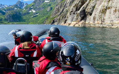 RIB boat tour in Lofoten with passengers in helmets, surrounded by mountains and water.