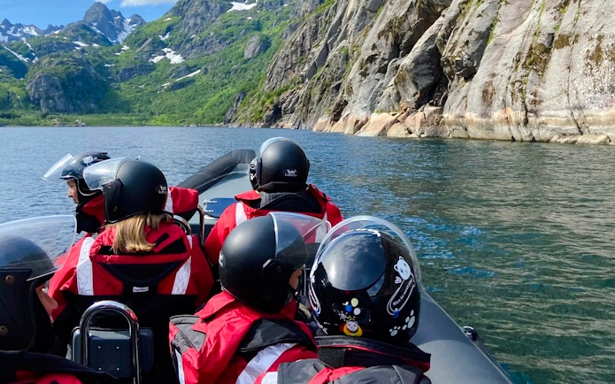 RIB boat tour in Lofoten with passengers in helmets, surrounded by mountains and water.