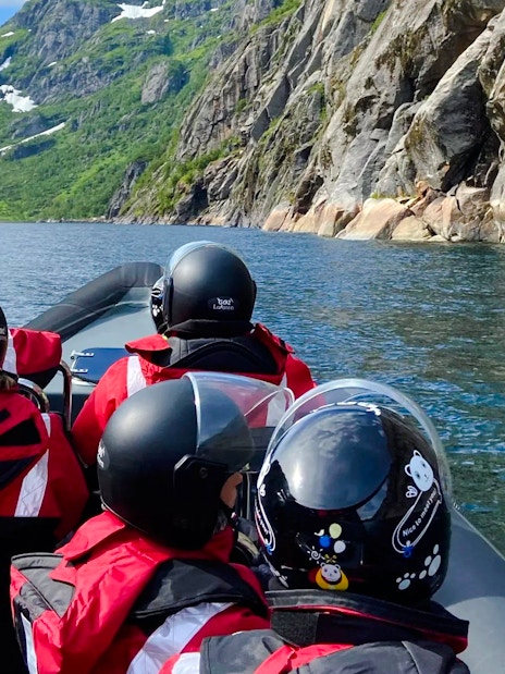 RIB boat tour in Lofoten with passengers in helmets, surrounded by mountains and water.