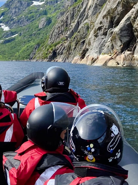 RIB boat tour in Lofoten with passengers in helmets, surrounded by mountains and water.