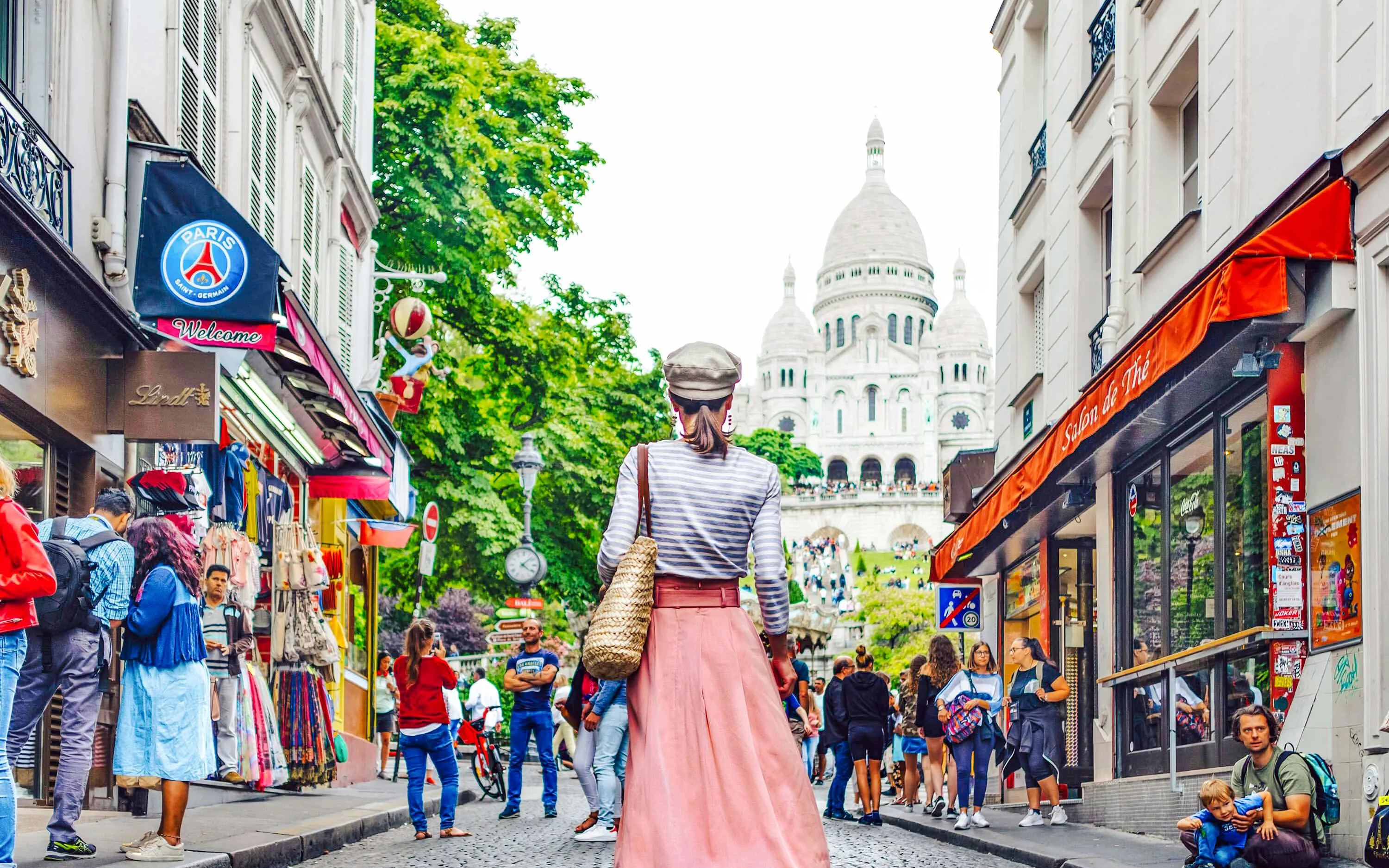 Tourists walking in Montmartre, Paris, with Sacré-Cœur Basilica in the background.