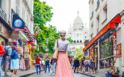 Tourists walking in Montmartre, Paris, with Sacré-Cœur Basilica in the background.