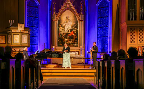 Performers at midnight concert in Tromsø Cathedral with illuminated altar backdrop.