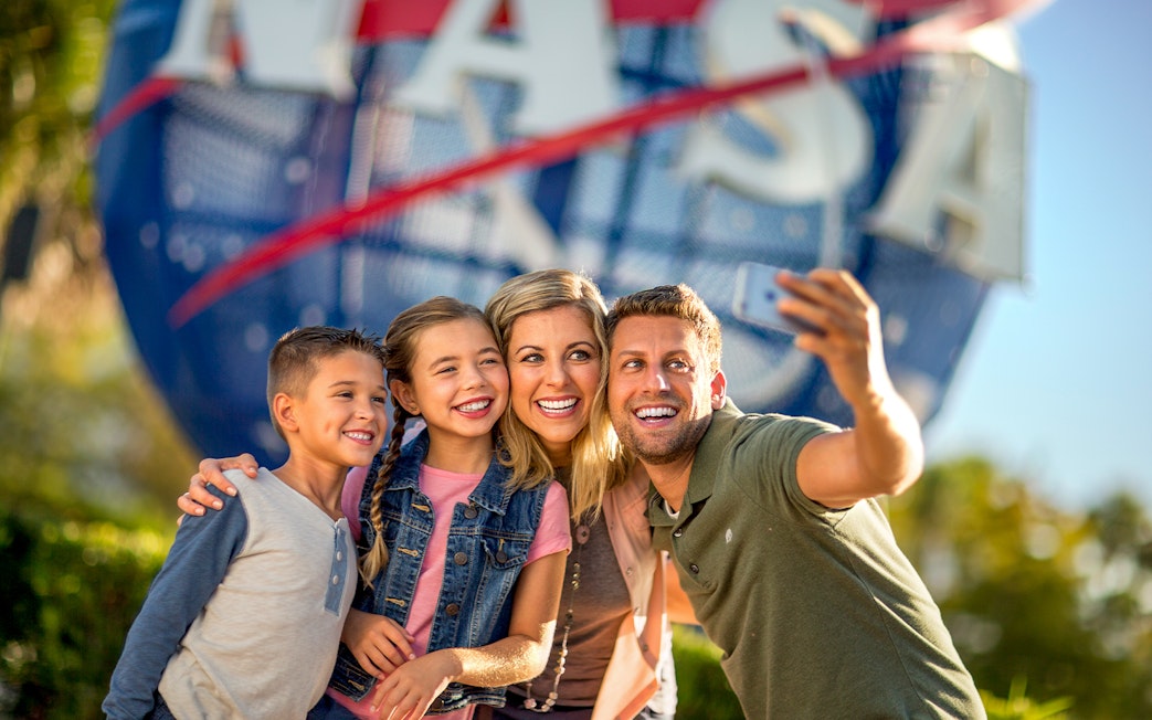 Visitors taking a selfie at Kennedy Space Center with NASA globe in background.