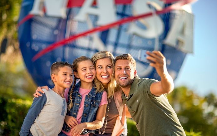 Visitors taking a selfie at Kennedy Space Center with NASA globe in background.