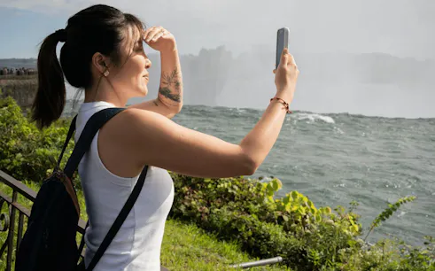 Tourist taking a photo at Niagara Falls during a guided tour with boat cruise, Canada.