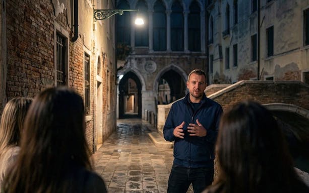 Guide leading tourists through a dimly lit alley in Venice.