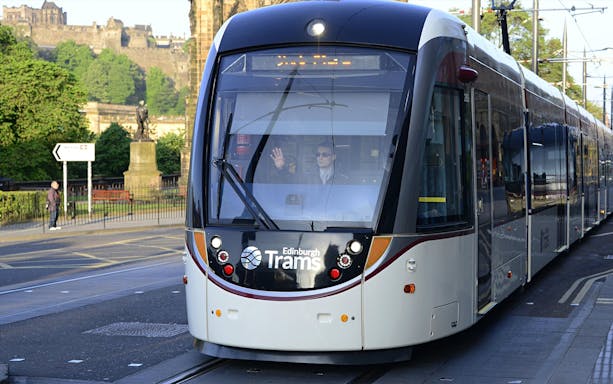 Edinburgh tram on route for airport transfer with cityscape in background.