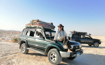 Safari vehicle in Black and White Desert, Cairo, with traveler sitting on hood.