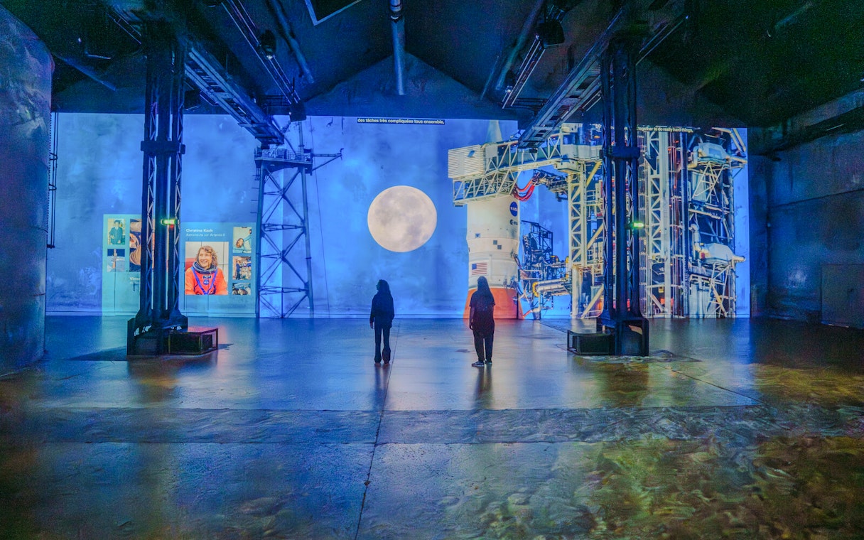 Visitors viewing lunar and space projections at The Moonwalkers Exhibition, Atelier des Lumières.