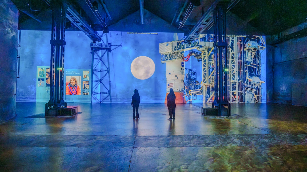 Visitors viewing lunar and space projections at The Moonwalkers Exhibition, Atelier des Lumières.