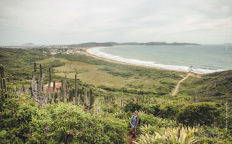 Hiker on a trail overlooking the coastline and greenery in Búzios, Rio de Janeiro.