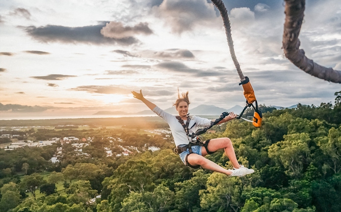 Person bungy jumping over lush landscape in Cairns, Australia at sunset.