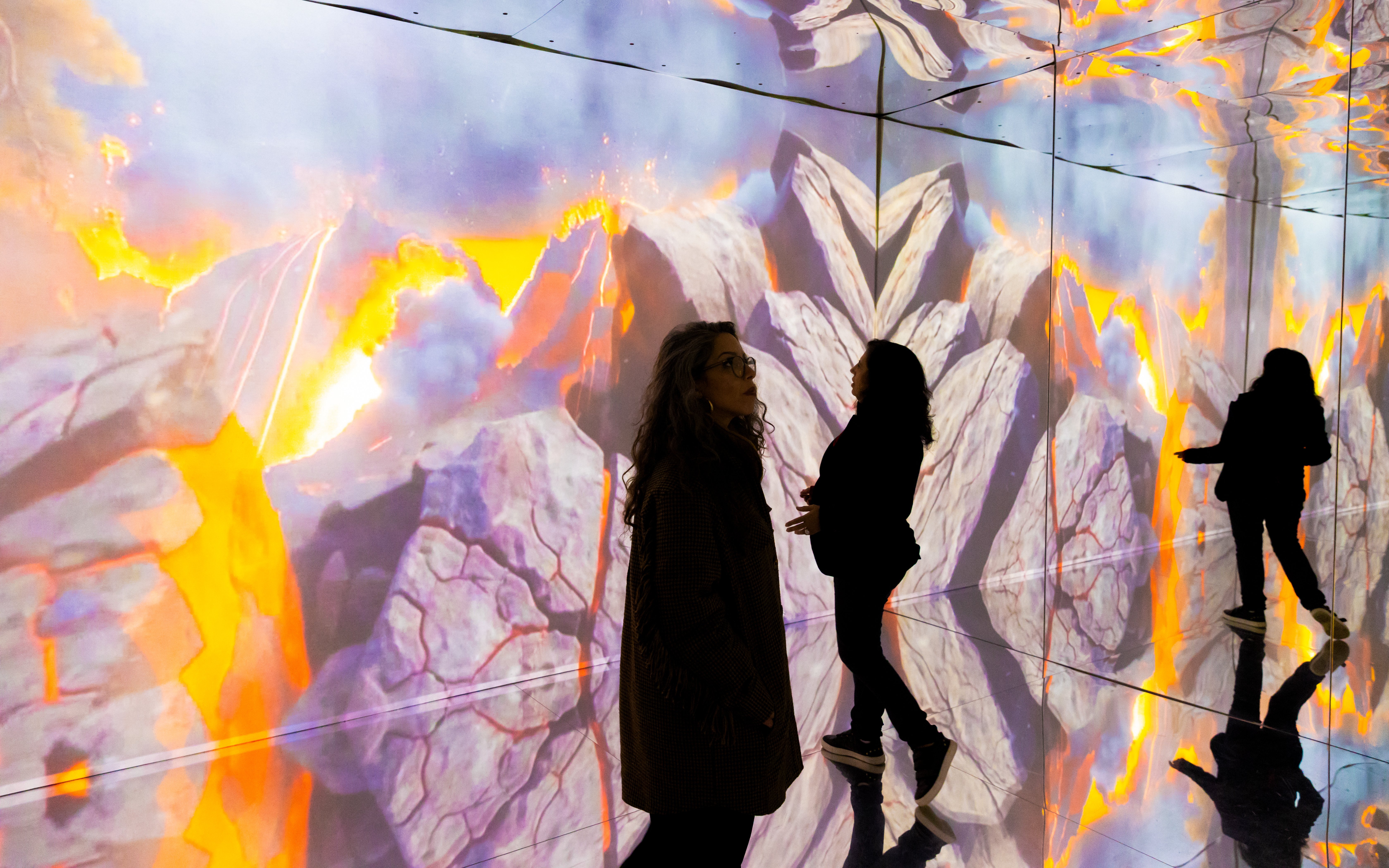 Tourists exploring immersive dinosaur exhibition with volcanic imagery in Porto.