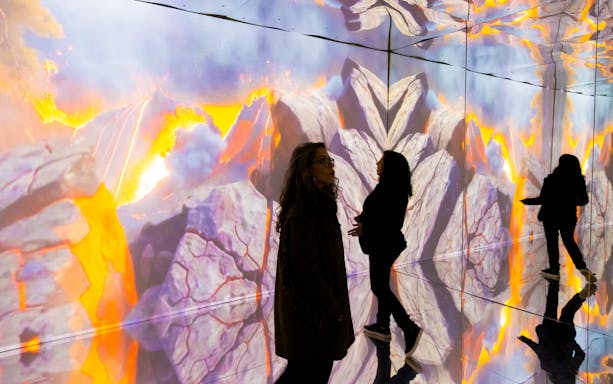 Tourists exploring immersive dinosaur exhibition with volcanic imagery in Porto.