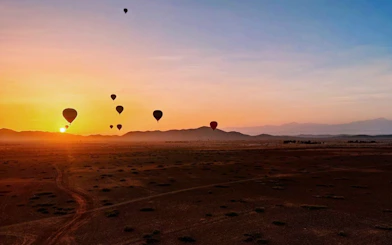 Hot air balloons at sunrise over Marrakesh desert landscape.