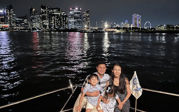 Family enjoying a yacht cruise with Marina Bay Sands and Singapore skyline in the background.