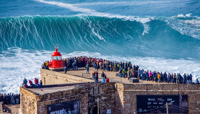 Nazare beach with crashing waves and surfers in Portugal.