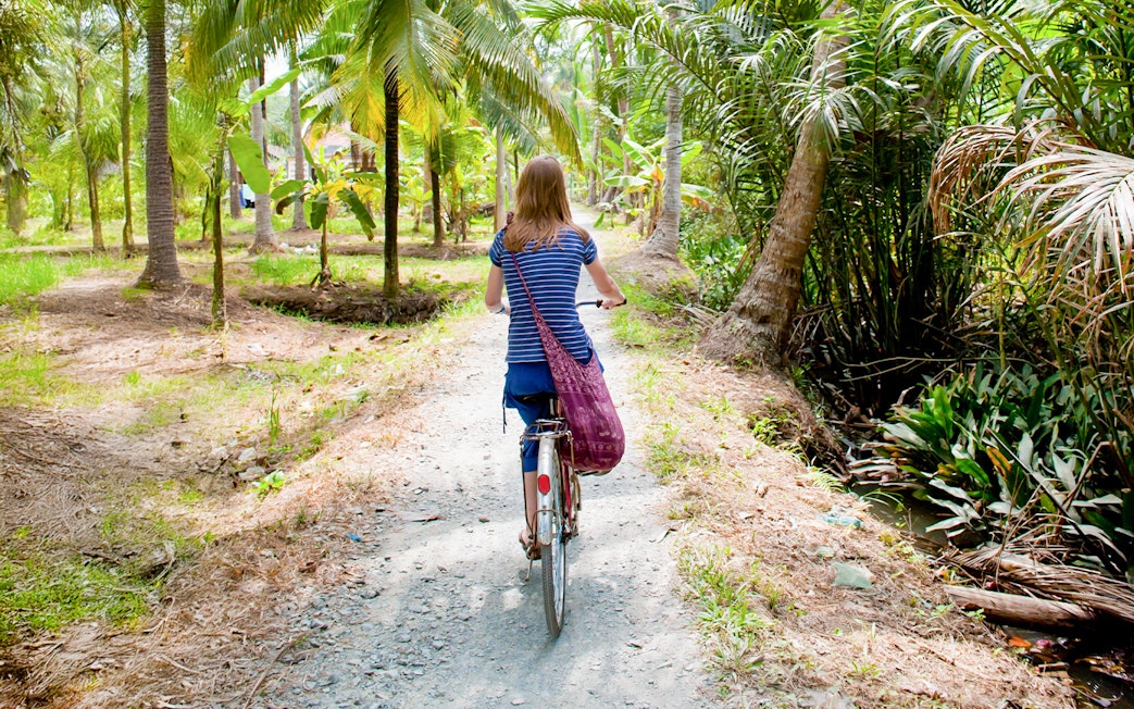 Tourist cycling through palm trees in My Tho, Mekong Delta.