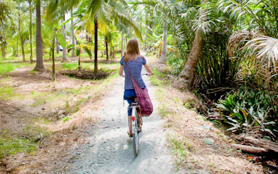 Tourist cycling through palm trees in My Tho, Mekong Delta.