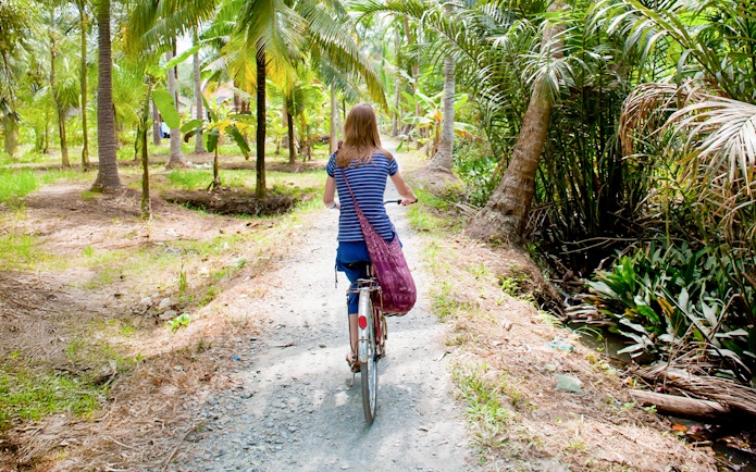 Tourist cycling through palm trees in My Tho, Mekong Delta.