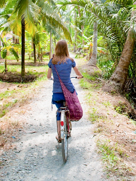 Tourist cycling through palm trees in My Tho, Mekong Delta.
