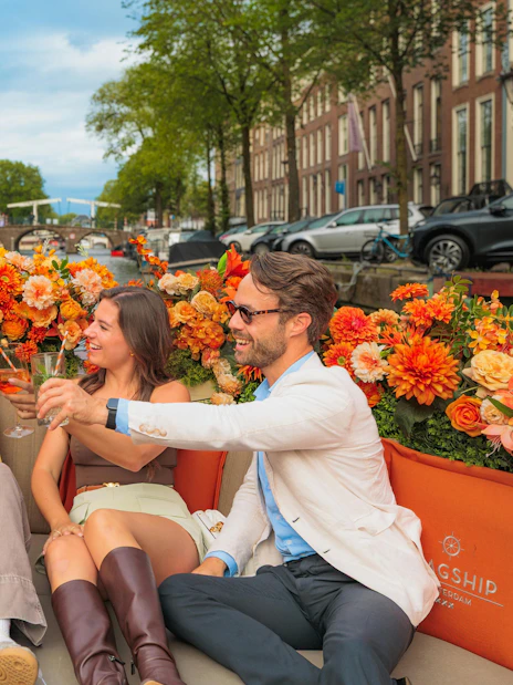 Guests enjoying drinks on a luxury boat canal cruise in Amsterdam with vibrant flowers.