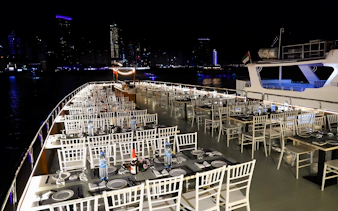 Dhow cruise dinner setup with tables and chairs on deck, Dubai Marina skyline at night.