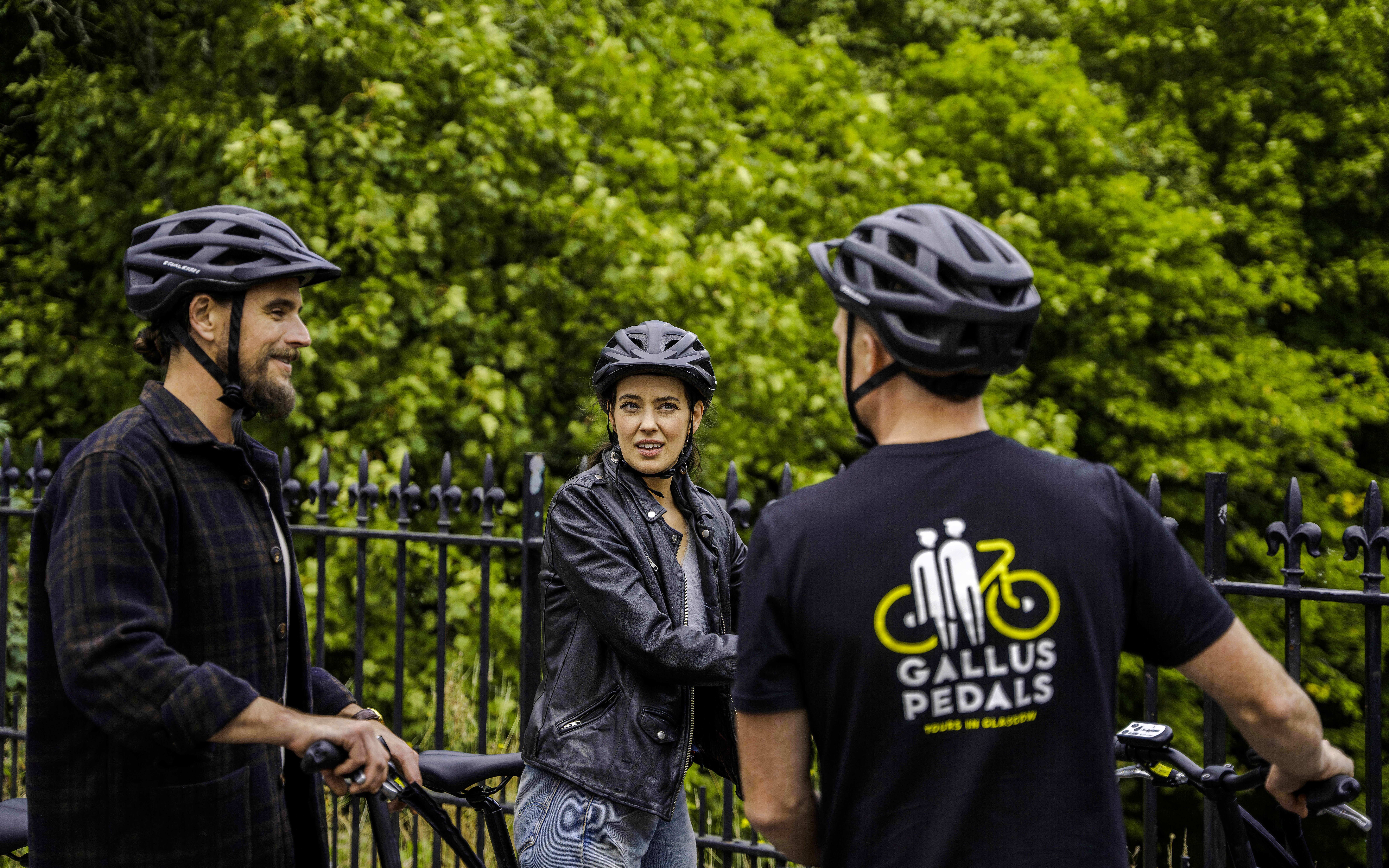 Guests on bikes during the Glasgow Highlights Bike Tour, stopped by a park fence.