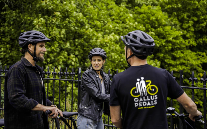 Guests on bikes during the Glasgow Highlights Bike Tour, stopped by a park fence.