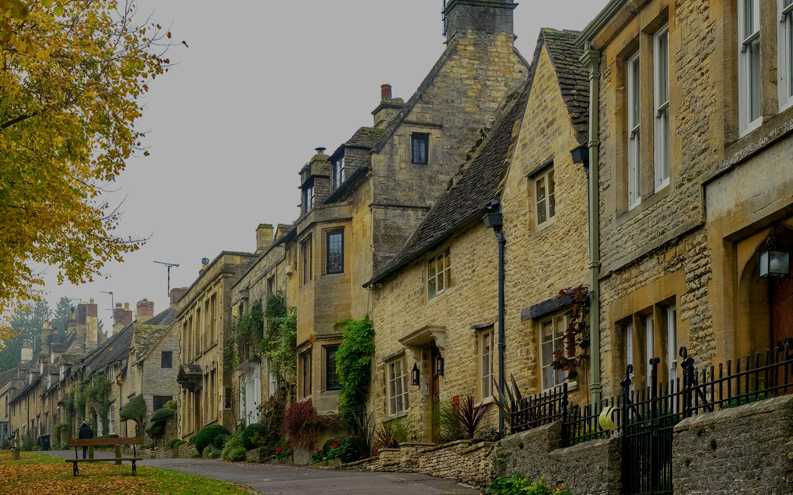 Burford street cottages with stone facades and autumn leaves in the Cotswolds, England.