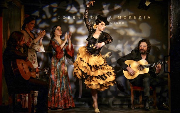 Flamenco dancer performing at Corral de la Morería with musicians and clapping audience.