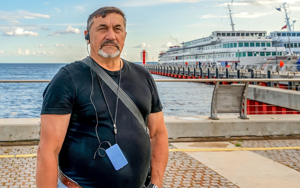 Man with audio guide at Hamburg harbor with docked ship in background.