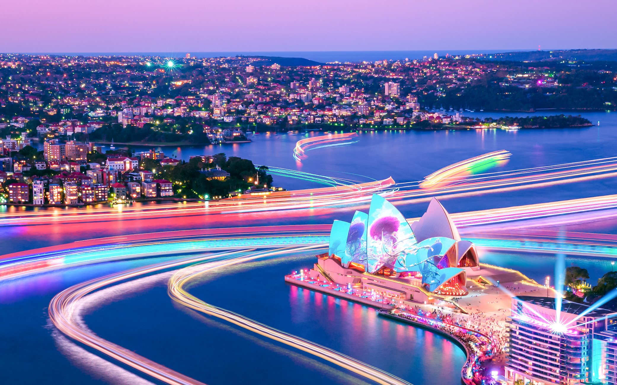 Sydney Opera House illuminated during Vivid Sydney cruise, with colorful light trails on the harbor.