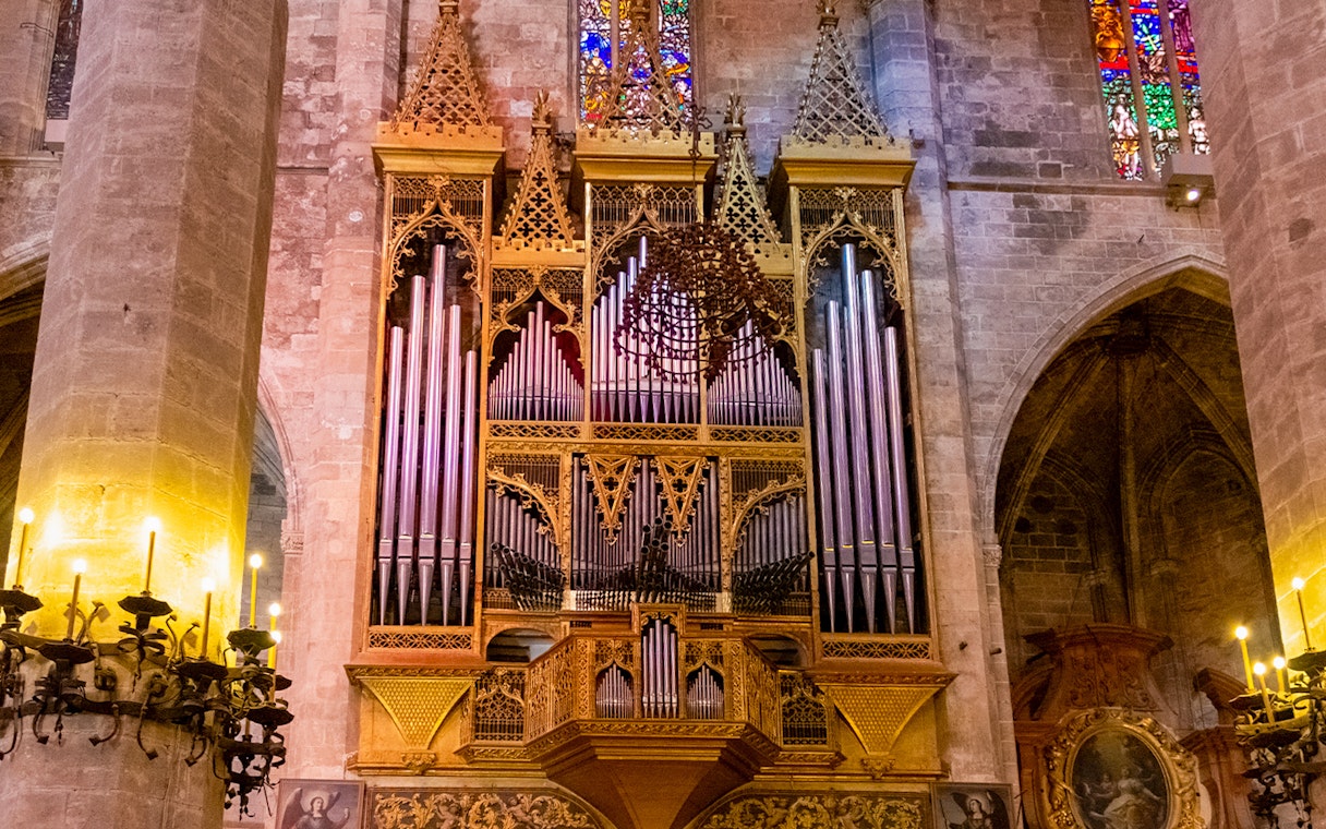 Organ inside Palma de Mallorca Cathedral with ornate pipes and stained glass backdrop.