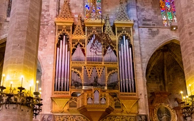 Organ inside Palma de Mallorca Cathedral with ornate pipes and stained glass backdrop.