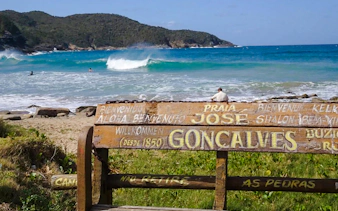 Bench overlooking José Gonçalves beach with waves and hills, Rio de Janeiro.