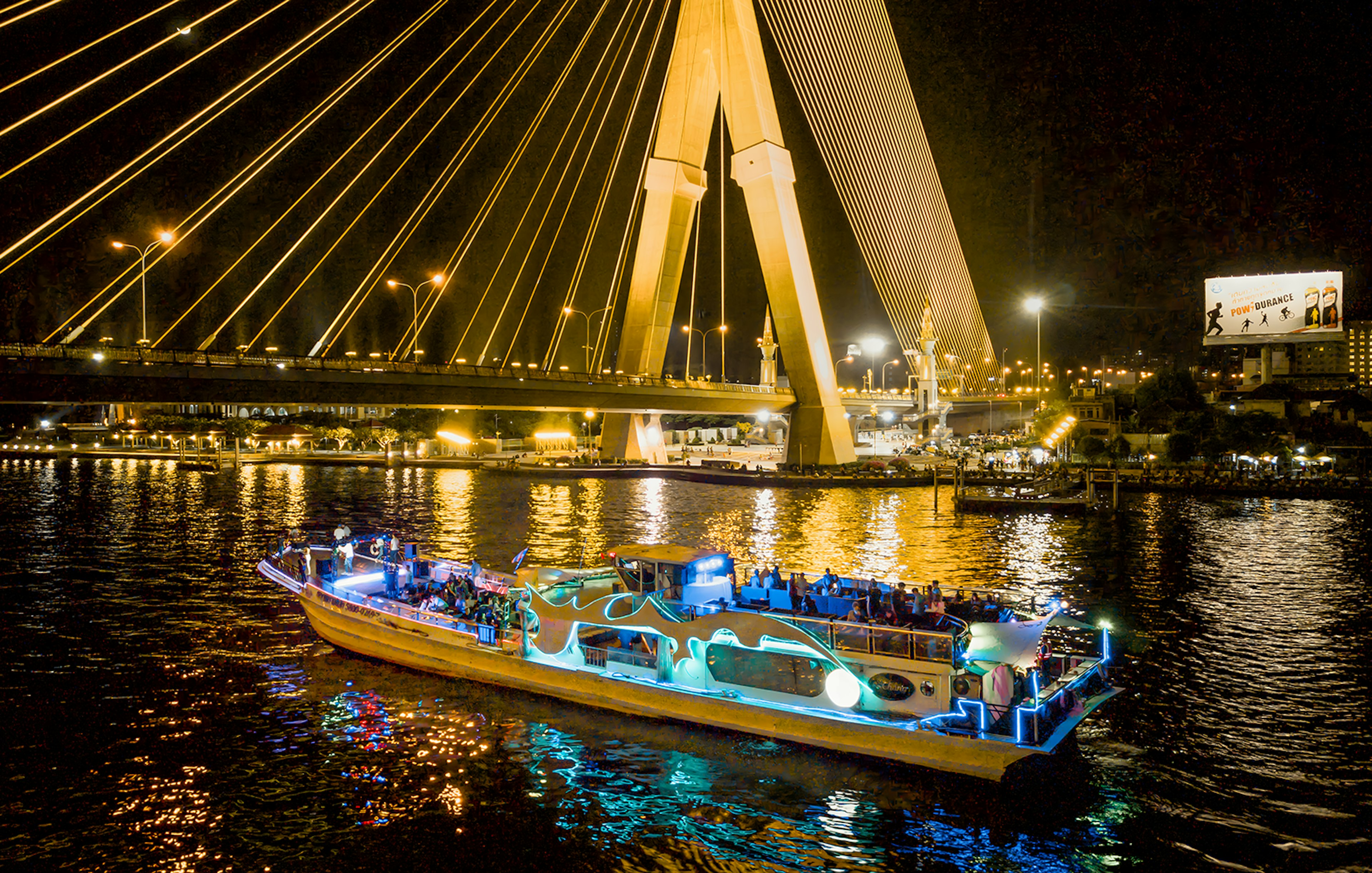 Yodsiam Sightseeing Boat at night under illuminated bridge in Bangkok.