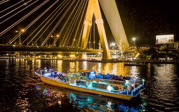 Yodsiam Sightseeing Boat at night under illuminated bridge in Bangkok.