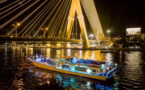 Yodsiam Sightseeing Boat at night under illuminated bridge in Bangkok.