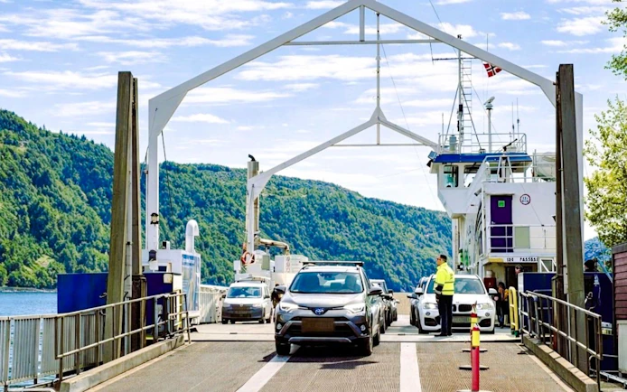 Cars boarding the Osteror ferry with scenic forested hills in the background.