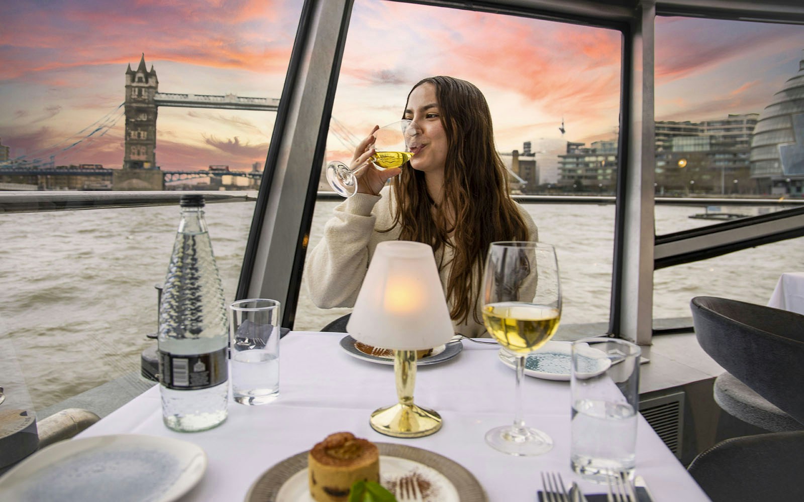 Dinner cruise guests dining on the River Thames with London skyline views.