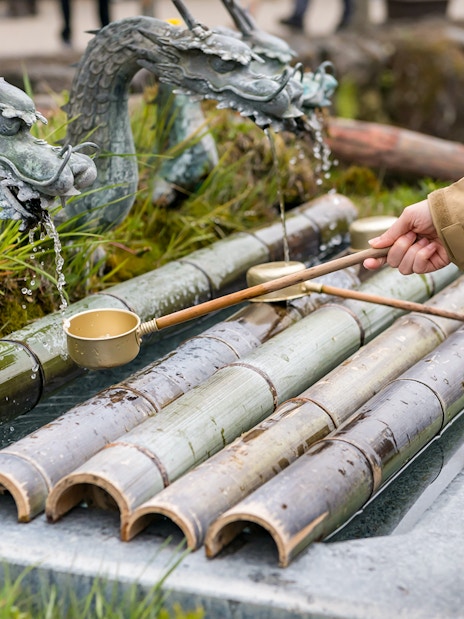 Person using a ladle at a traditional purification fountain in Tokyo.