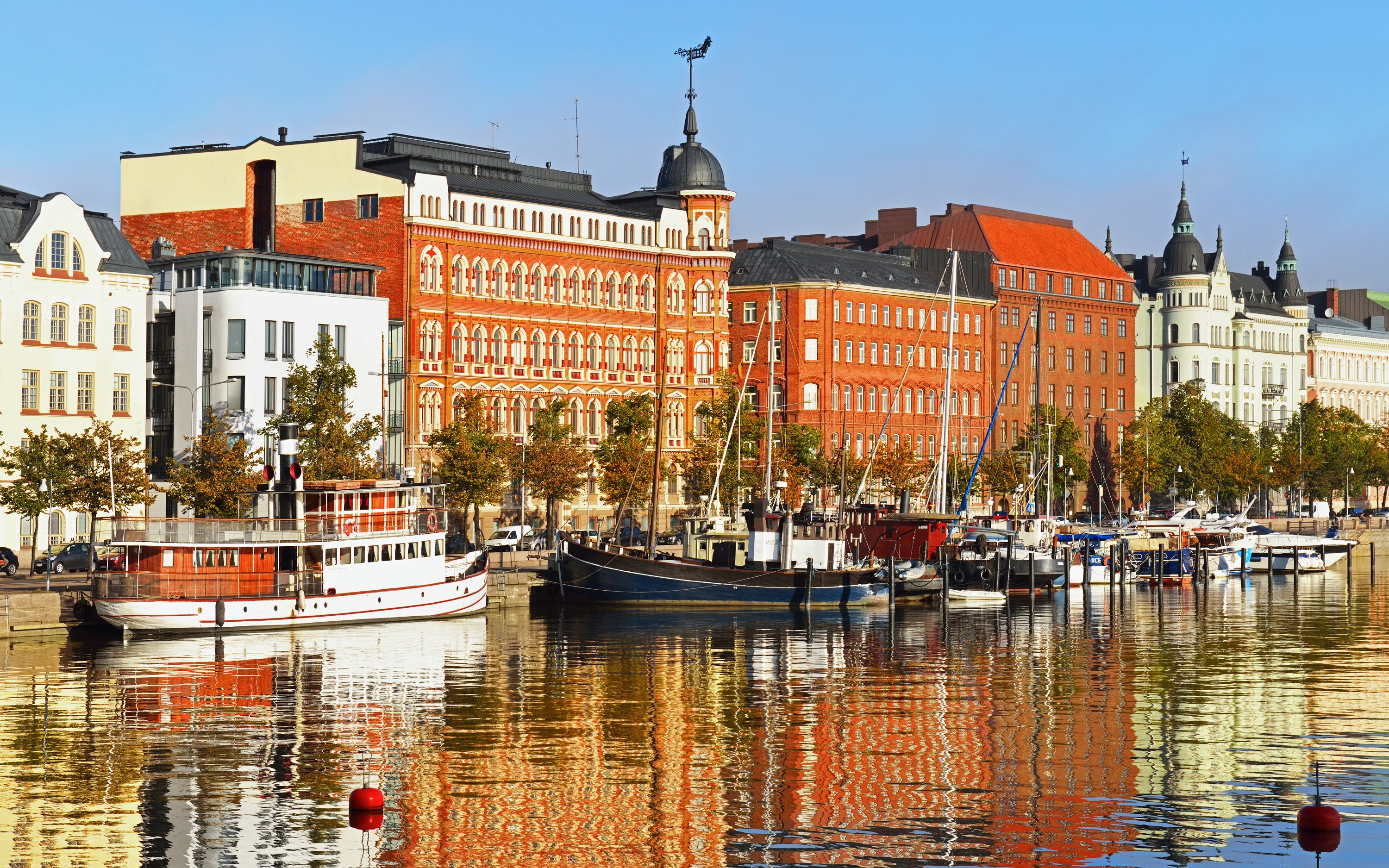 Helsinki harbor with boats and historic buildings reflecting on the water, Finland.