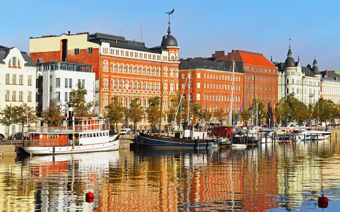 Helsinki harbor with boats and historic buildings reflecting on the water, Finland.