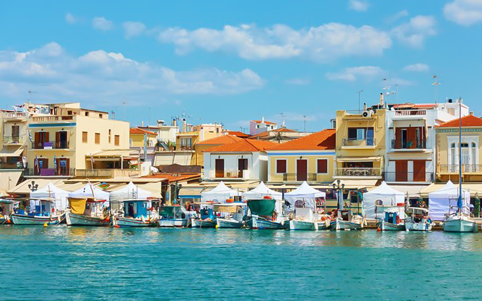 Boats docked at the port of Aegina Town with colorful buildings in the background.