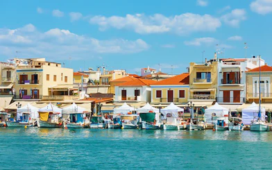 Boats docked at the port of Aegina Town with colorful buildings in the background.