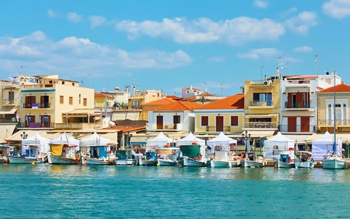 Boats docked at the port of Aegina Town with colorful buildings in the background.