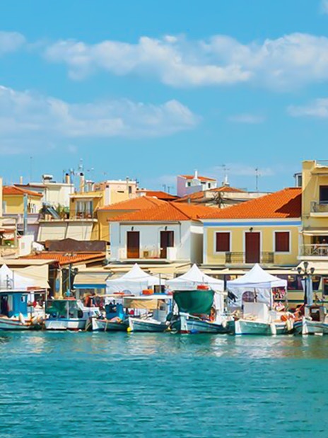 Boats docked at the port of Aegina Town with colorful buildings in the background.
